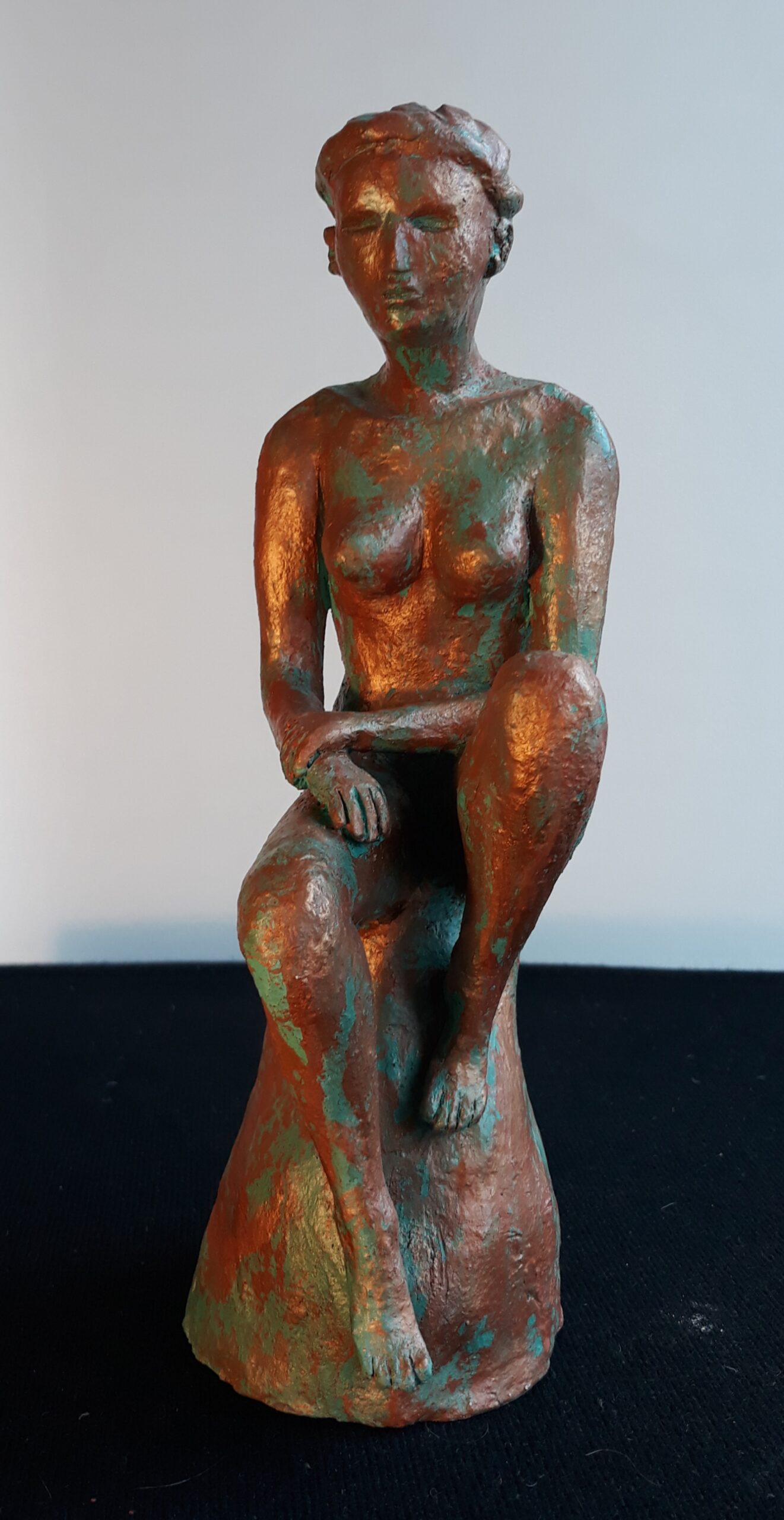 Sculpture de Patrick Voisin représentant une Femme nue assise sur un rocher. Vue de face.