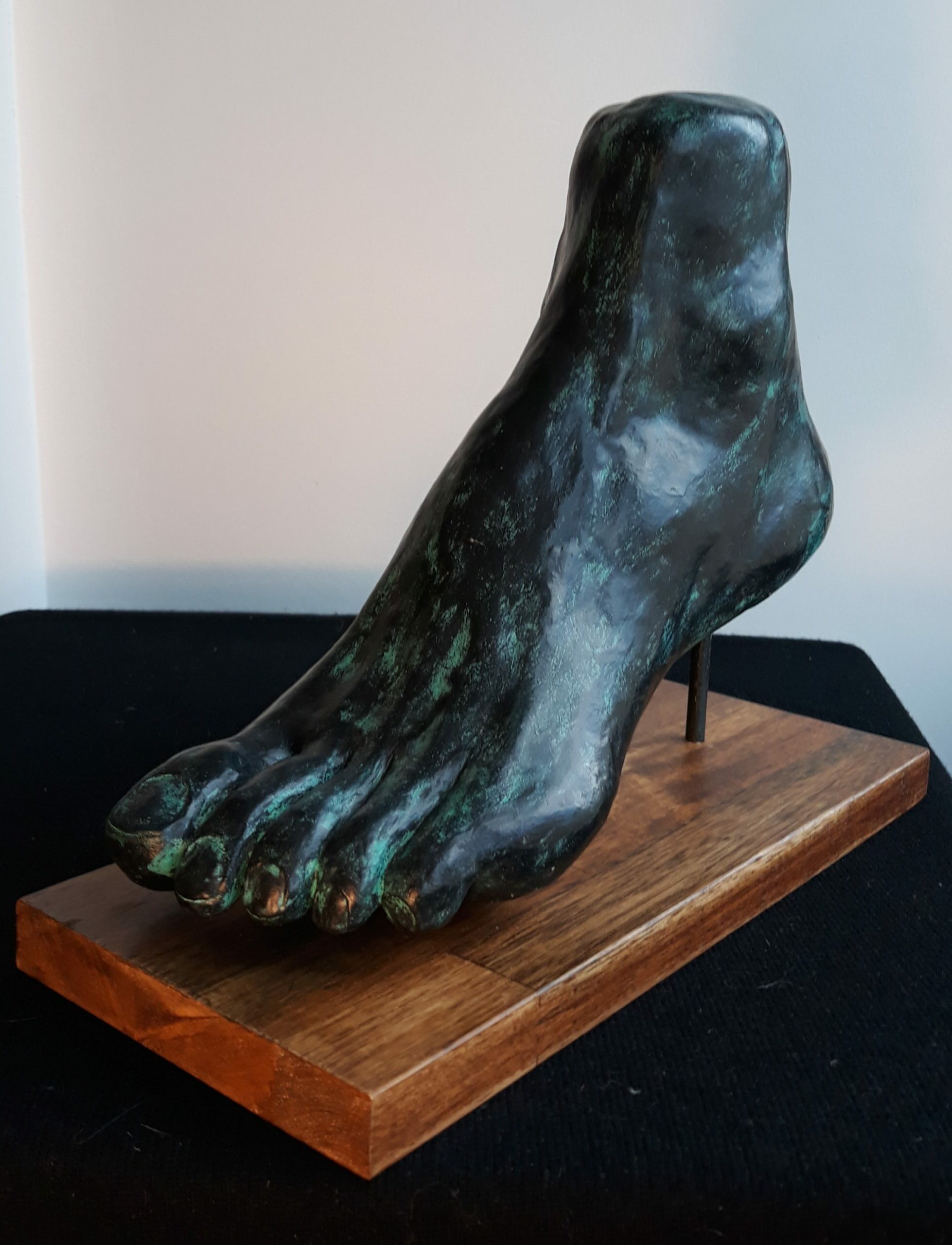 Sculpture de Patrick Voisin représentant un pied gauche en terre cuite, patine à la colle à bois, pigments blancs, verts et noirs pour un effet bronze, finition au vernis, sur socle bois. Vue côté extérieur.