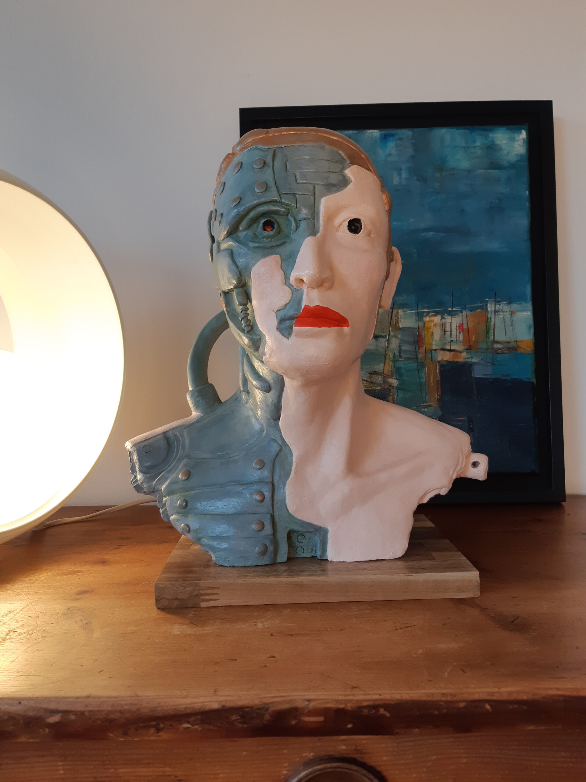 Sculpture de Patrick Voisin. Terre cuite représentant une tête de cyborg. Patine à la peinture acrylique blanche, orange, bleu, verte, brune et dorée, finition à la cire. Vue de face.