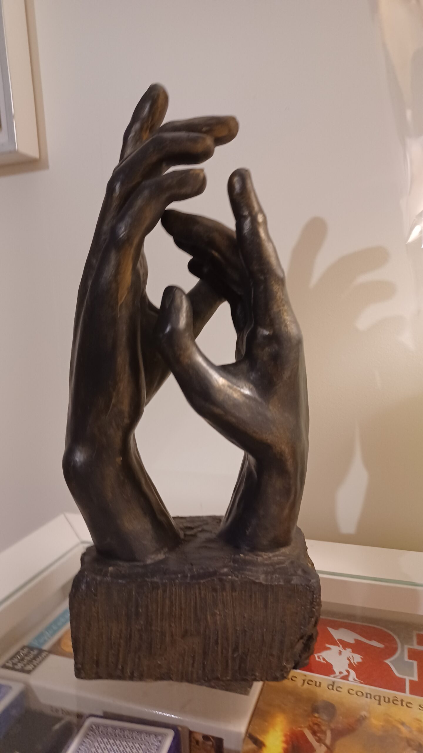 Sculpture de Patrick Voisin, intitulée "Génération", représentant 2 mains, une garnde et une plus petite, se faisant face. Terre cuite, patine à la peinture acrylique noire, brune foncée et dorée, finition au vernis. Vue de côté, grande main à gauche.